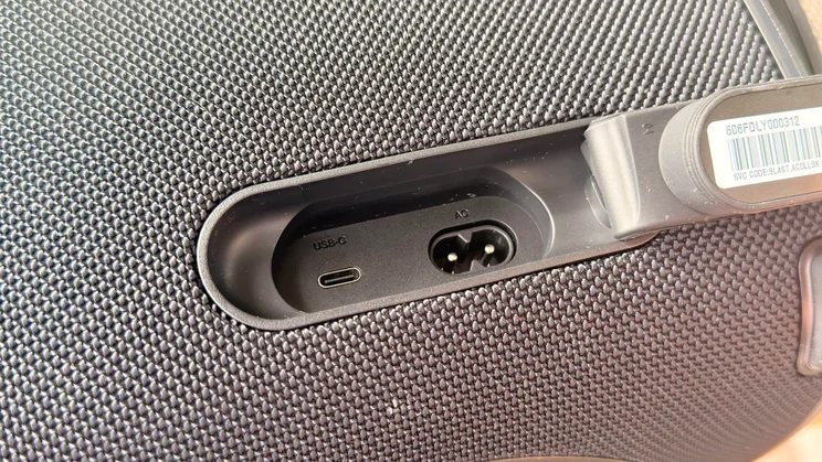 A close-up shot of the rear port compartment on the LG xboom Blast speaker with its protective flap pulled open, exposing a USB-C port and an AC power input port