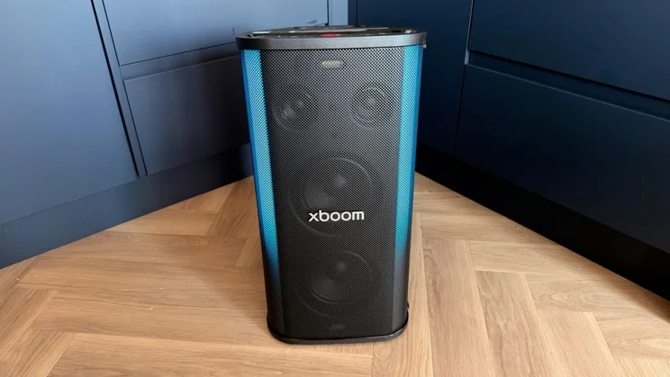 A front view of the upright LG xboom Stage 501 party speaker displaying vibrant blue side lighting on a wooden floor