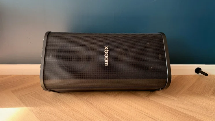 The LG xboom Stage 501 speaker positioned horizontally on a wooden herringbone floor against a dark wall