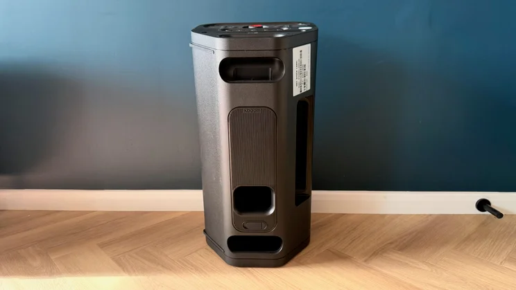 A rear view of the upright LG xboom Stage 501 speaker resting on a light wooden floor against a dark wall