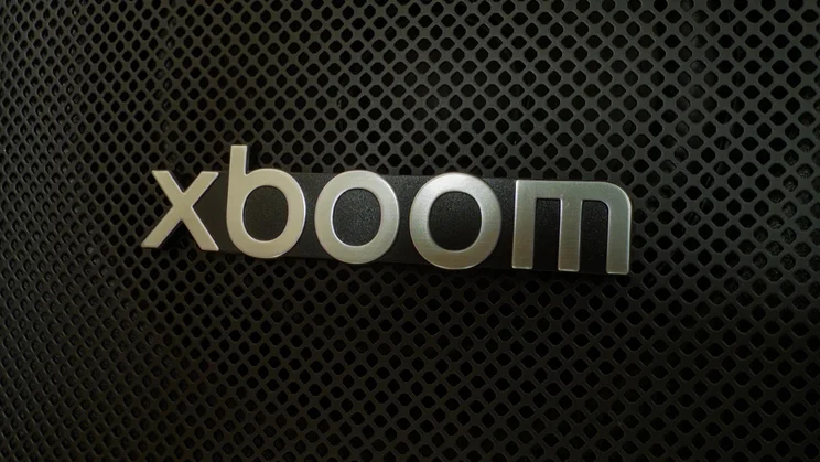 A detailed macro close-up of the silver xboom branding badge on the front speaker grille of the LG xboom Stage 501
