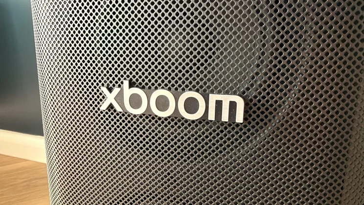 A close-up view of the metallic xboom logo mounted on the front mesh grille of the LG xboom Stage 501 speaker, with the speaker driver subtly visible behind
