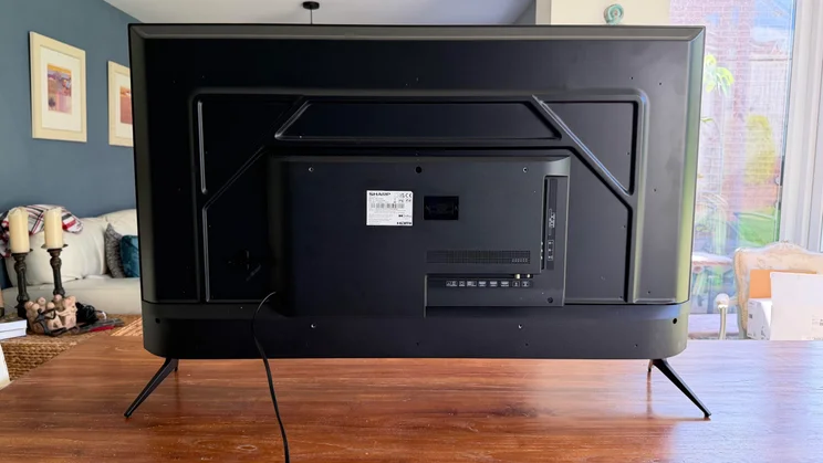 Full rear view of the Sharp HJ6725KB Roku TV showing the complete back panel, centre casing box with ports, stand legs, and power cable