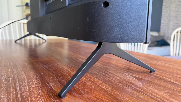 Low-angle rear view of the Sharp HJ6725KB Roku TV highlighting the black V-shaped stand legs resting on a polished wooden surface