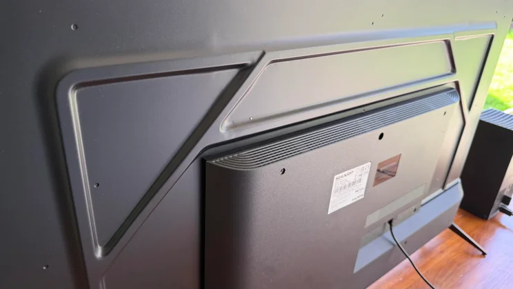 Close-up rear view of the Sharp HJ6725KB Roku TV highlighting the textured back panel, geometric casing lines, mounting holes, product information label, and cable connection port