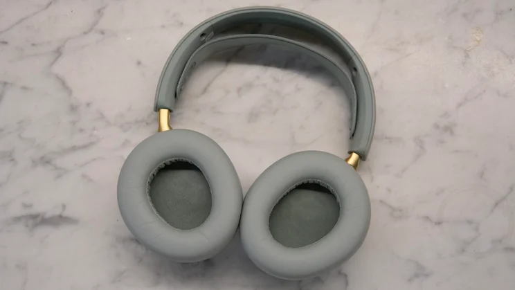 The SteelSeries Arctis Nova Elite gaming headset lying flat on a marble background with the soft grey-green fabric ear cushions facing upward