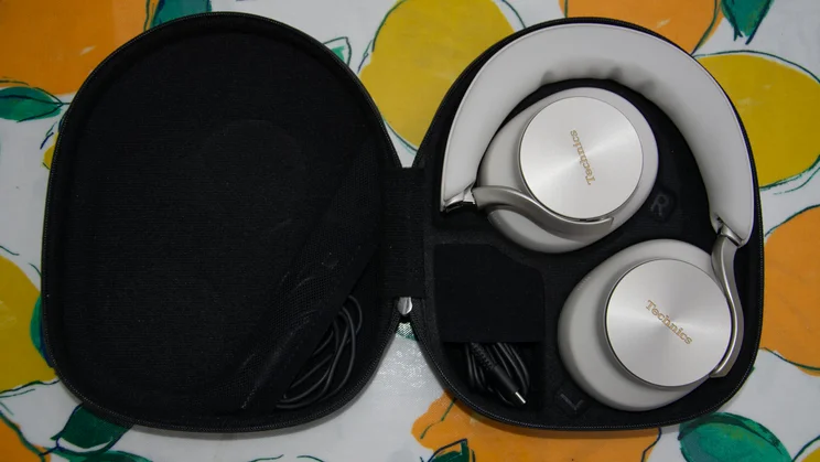 Technics EAH-A1000 headphones folded neatly inside the open black carrying case with bundled audio and charging cables in their storage compartment