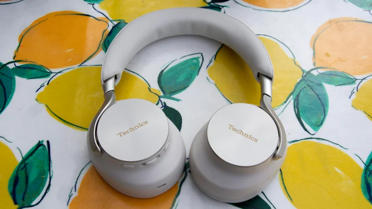 Technics EAH-A1000 headphones resting earcups-down on a lemon-patterned background, showcasing the silver exterior caps with embossed branding and edge control buttons