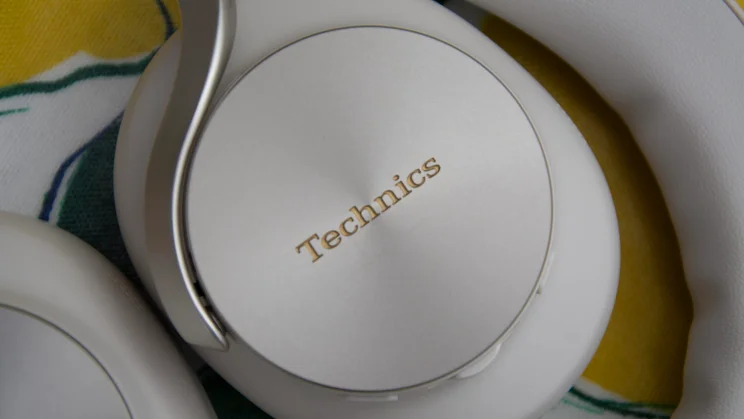 Close-up shot of the circular, brushed metal exterior ear cup of the Technics EAH-A1000 featuring the gold-coloured embossed Technics brand logo