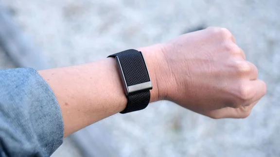 Whoop 5.0 worn on a raised wrist, showing the black woven elastic band and gunmetal metal slider from above