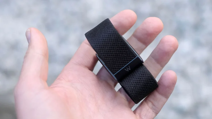 Whoop 5.0 band held in an open palm, with the engraved logo on the case and the textured black band visible