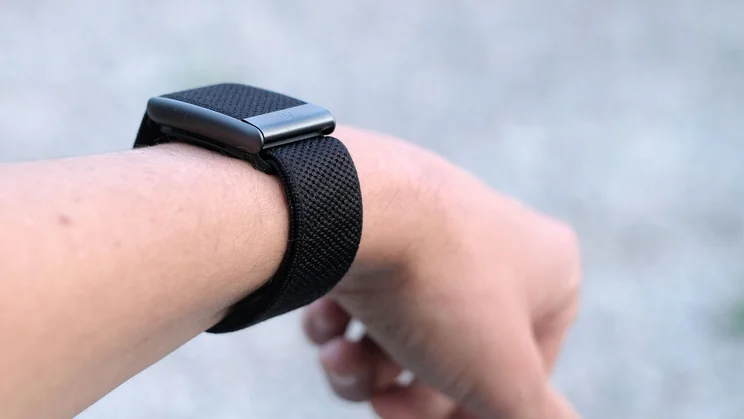 Angled view of a Whoop 5.0 on the wrist, with the textured black band wrapped around the forearm below the case