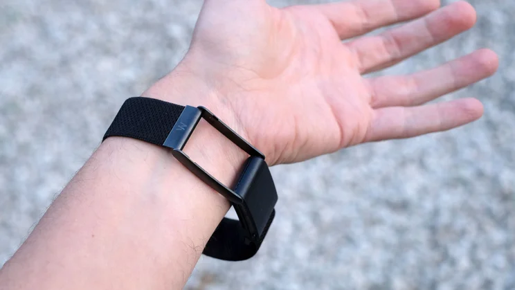Inner-wrist view of a Whoop 5.0 with the open metal case loop and sensor pod beside the black band, palm facing up