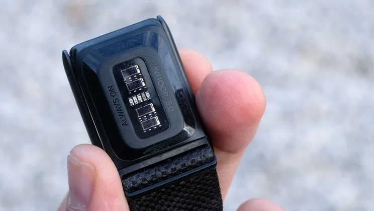 Underside of a Whoop 5.0 held between fingers, showing the optical sensors and Whoop 5.0 markings