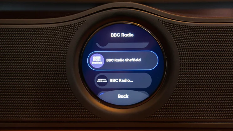 Close-up of the circular display on the front of the WiiM Bar soundbar, showing a menu selection for BBC Radio stations