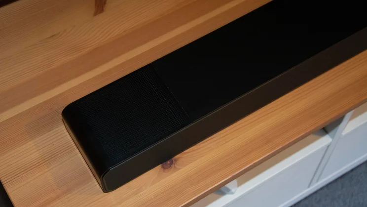 Top-down angled view of the left end of the black WiiM Bar soundbar resting on a light wood surface.