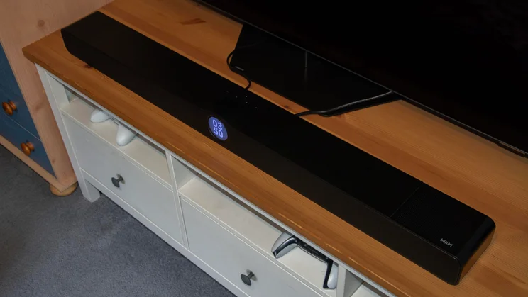 High-angle view looking down at the full length of the black WiiM Bar soundbar sitting on a wooden media stand